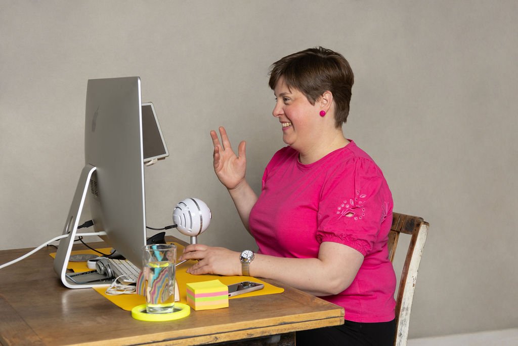 Lou, a white woman with short dark hair, wearing a pink top, sat at her computer on a video call with her microphone.